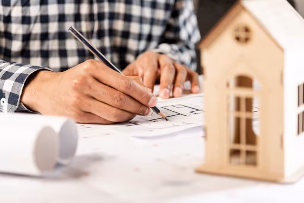 Architect drafting blueprint with wooden house model.